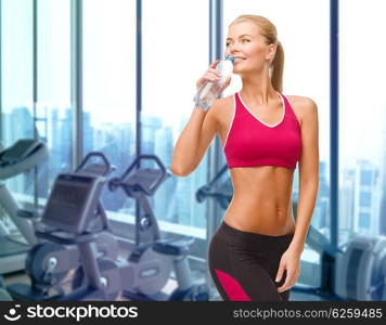 people, sport, fitness and recreation concept - happy woman drinking water from bottle over gym machines background