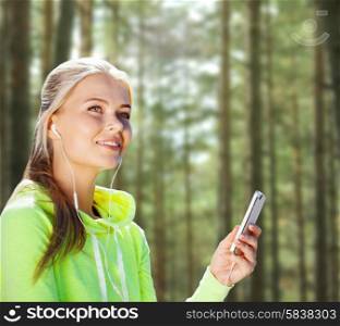 people, sport, fitness and technology concept - happy woman with smartphone and earphones listening to music over woods background