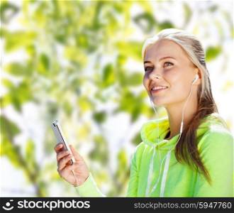people, sport, fitness and technology concept - happy woman with smartphone and earphones listening to music over green tree leaves background