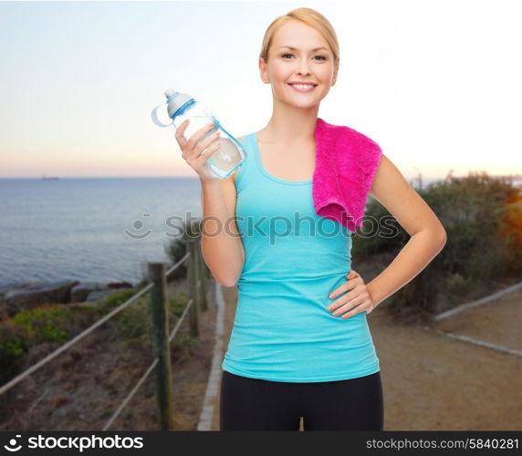 people, sport, fitness, jogging and recreation concept - happy woman with bottle of water and towel over beach sunset background