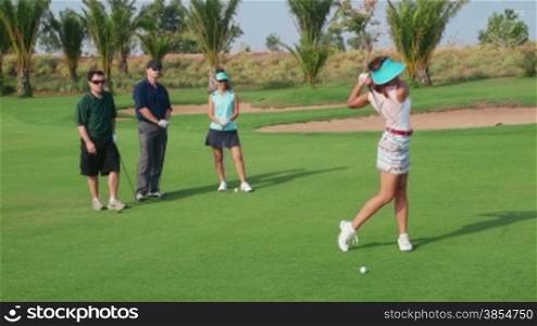 People, sport, leisure activities, recreation and lifestyle, golf in country club during summer holidays. Asian woman playing golf near hole, group of friends watching. 10of30