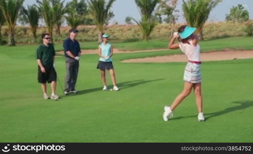 People, sport, leisure activities, recreation and lifestyle, golf in country club during summer holidays. Asian woman playing golf near hole, group of friends watching. 10of30