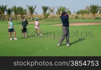 People, sport, leisure activity, recreation and lifestyle, golf in country club during summer holiday. Man playing golf near hole, group of friends watching. 9of30