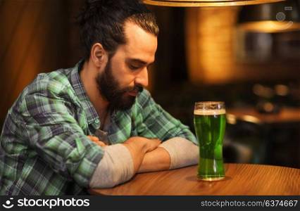 people, st patricks day and alcohol concept - unhappy single man with beard drinking green beer at bar or pub. lonely man drinking green beer at bar or pub