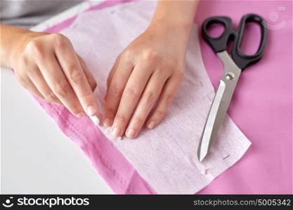 people, stitching, needlework and tailoring concept - tailor woman with paper pattern and chalk drawing on fabric at sewing studio. woman with pattern and chalk drawing on fabric