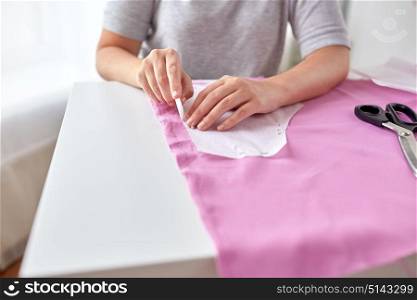 people, stitching, needlework and tailoring concept - tailor woman with paper pattern and chalk drawing on fabric at sewing studio. woman with pattern and chalk drawing on fabric