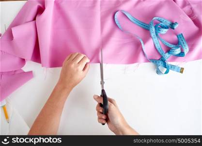 people, stitching, needlework, sewing and tailoring concept - woman with tailor scissors or shears cutting out fabric at studio. woman with tailor scissors cutting out fabric