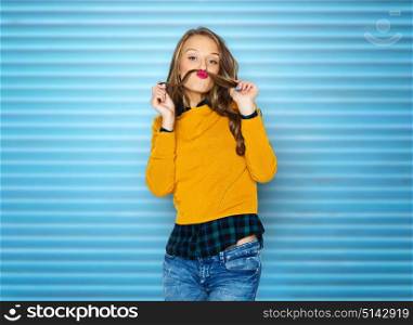people, style and fashion concept - happy young woman or teen girl in casual clothes having fun making mustache of her hair strand over blue ribbed wall background. happy young woman or teen girl in casual clothes
