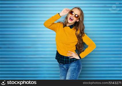 people, style and fashion concept - happy young woman or teen girl in casual clothes and sunglasses having fun over blue ribbed wall background. happy young woman or teen girl in casual clothes