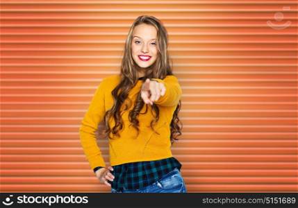 people, style and fashion concept - happy young woman or teen girl in casual clothes pointing finger to you over orange ribbed wall background. happy young woman or teen pointing finger to you