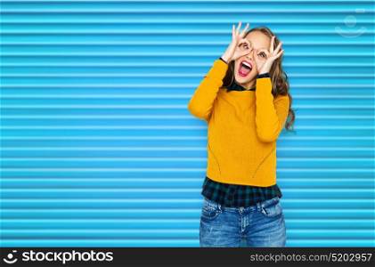people, style and fashion concept - happy young woman or teen girl in casual clothes having fun and making finger glasses over blue ribbed background. happy young woman or teen girl having fun
