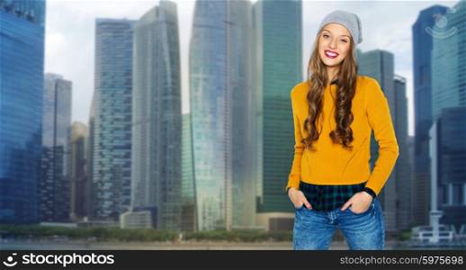 people, style and fashion concept - happy young woman or teen girl in casual clothes and hipster hat over singapore city background