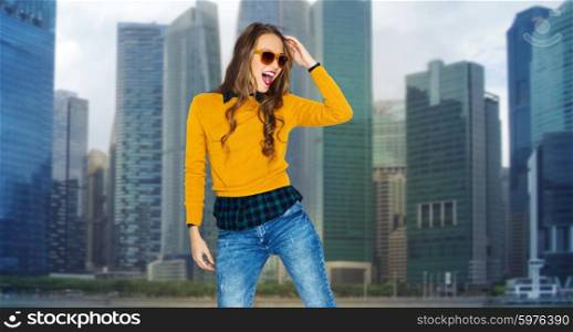 people, style and fashion concept - happy young woman or teen girl in casual clothes and sunglasses having fun over singapore city background