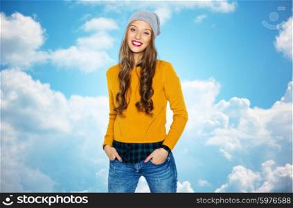 people, style and fashion concept - happy young woman or teen girl in casual clothes and hipster hat over blue sky and clouds background