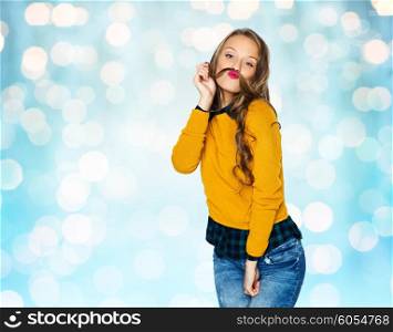 people, style and fashion concept - happy young woman or teen girl in casual clothes having fun and making mustache of her hair strand over blue holidays lights background