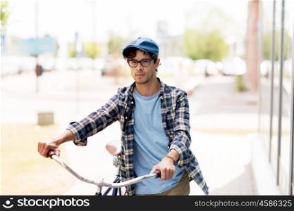 people, style, city life and lifestyle - young hipster man in vintage cap and fixed gear bicycle walking along city on street