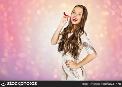 people, style, holidays, celebration and fashion concept - happy young woman or teen girl in fancy dress with sequins and party horn over rose quartz and serenity lights background