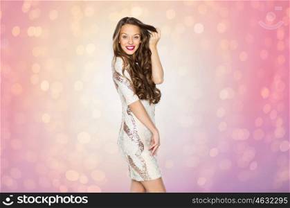 people, style, holidays, hairstyle and fashion concept - happy young woman or teen girl in fancy dress with sequins touching long wavy hair over rose quartz and serenity lights background