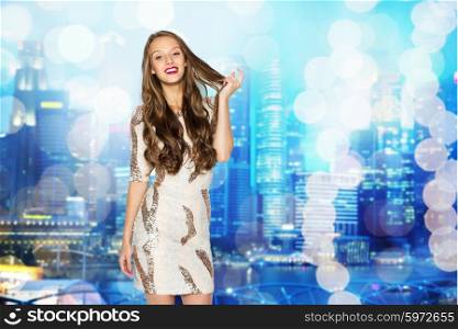 people, style, holidays, hairstyle and fashion concept - happy young woman or teen girl in fancy dress with sequins touching long wavy hair
