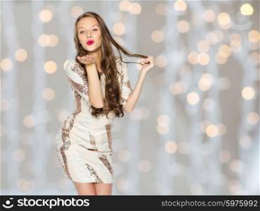 people, style, holidays, hairstyle and fashion concept - happy young woman or teen girl in fancy dress with sequins and long wavy hair sending blow kiss over lights background
