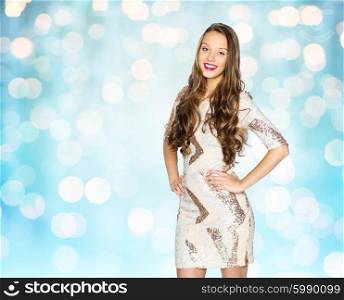 people, style, holidays, hairstyle and fashion concept - happy young woman or teen girl in fancy dress with sequins and long wavy hair over blue lights background