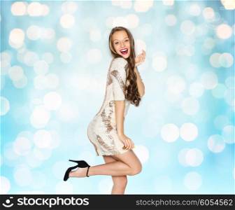 people, style, holidays, hairstyle and fashion concept - happy young woman or teen girl in fancy dress with sequins and long wavy hair posing over blue lights background