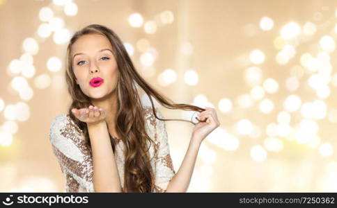 people, style, holidays, hairstyle and fashion concept - happy young woman or teen girl in fancy dress with sequins and long wavy hair sending blow kiss over festive lights background. happy young woman or teen girl in fancy dress