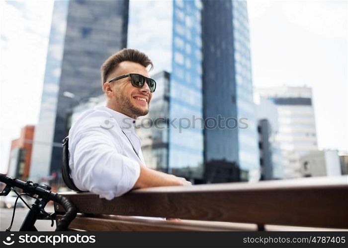 people, style, leisure and lifestyle - happy smiling young man with bicycle sitting on city bench