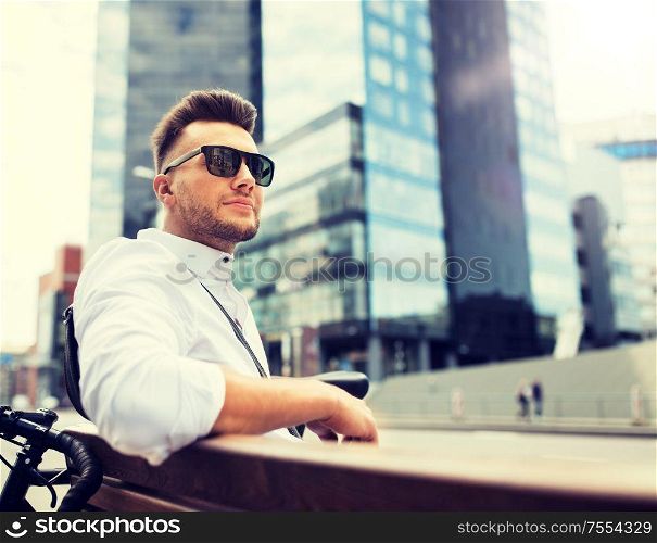 people, style, leisure and lifestyle - happy smiling young man with bicycle sitting on city bench. happy young man with bicycle sitting on city bench