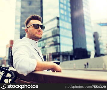 people, style, leisure and lifestyle - happy smiling young man with bicycle sitting on city bench. happy young man with bicycle sitting on city bench