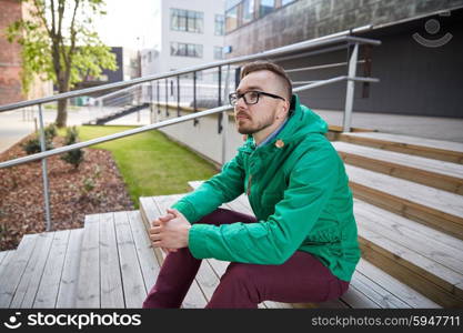 people, style, leisure and lifestyle - happy young hipster man in eyeglasses and jacket sitting on stairs in city