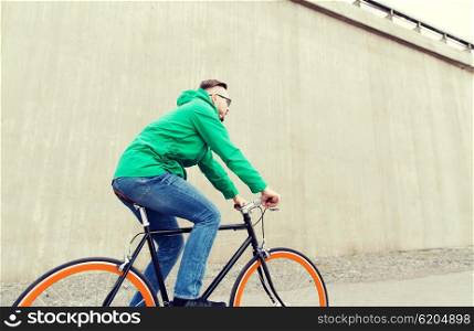 people, style, leisure and lifestyle - happy young hipster man riding fixed gear bike on city street