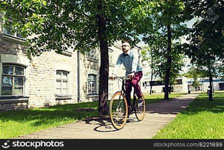 people, style, leisure and lifestyle - happy young hipster man riding fixed gear bike on city street