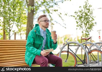 people, style, leisure and lifestyle - happy young hipster man with coffee cup and sandwich eating and drinking on city street