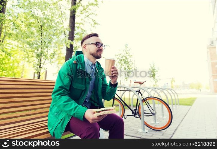 people, style, leisure and lifestyle - happy young hipster man with sandwich, coffee cup and fixed gear bike parked on city street