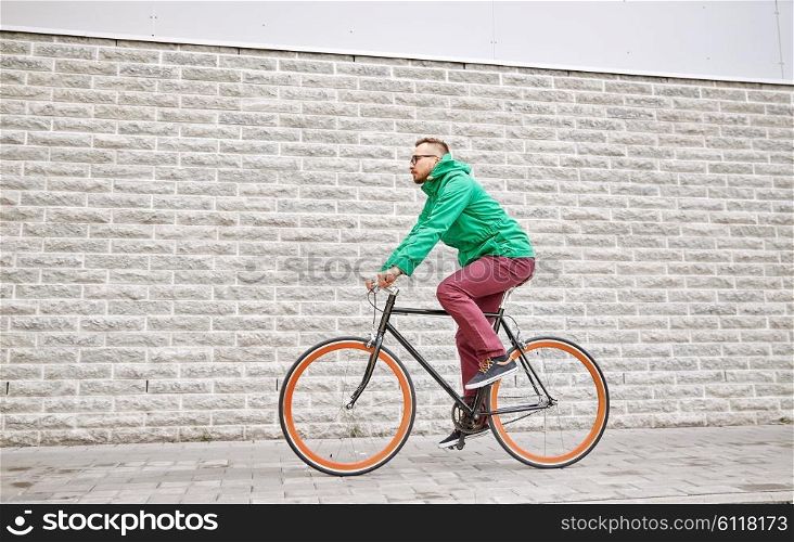 people, style, leisure and lifestyle - young hipster man riding fixed gear bike on city street over brick wall background