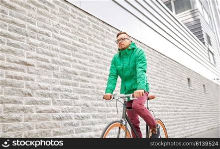 people, style, leisure and lifestyle - young hipster man riding fixed gear bike on city street over building brick wall background