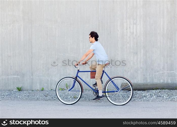 people, style, leisure and lifestyle - young hipster man riding fixed gear bike on city street