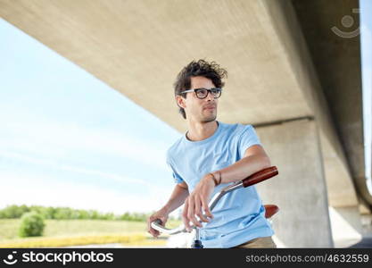 people, style, leisure and lifestyle - young hipster man riding fixed gear bike on city street