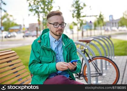 people, style, technology and lifestyle - happy young hipster man with smartphone and fixie bike sitting on bench in city