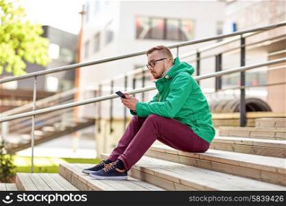people, style, technology and lifestyle - young hipster man with smartphone sitting on stairs in city