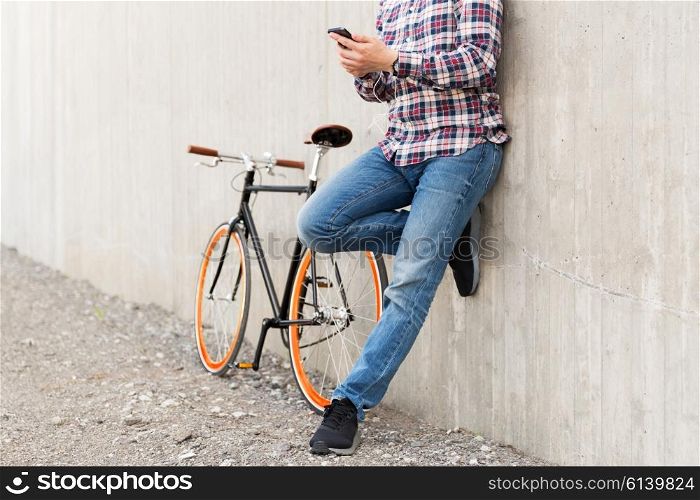 people, style, technology, leisure and lifestyle - close up of young hipster man in earphones with smartphone and fixed gear bike listening to music on city street