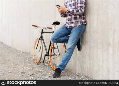people, style, technology, leisure and lifestyle - close up of young hipster man in earphones with smartphone and fixed gear bike listening to music on city street