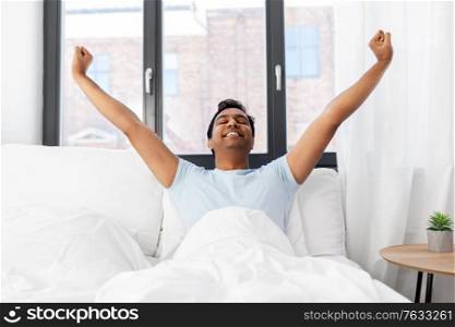 people, success and rest concept - happy smiling indian man lying in bed at home. happy smiling indian man lying in bed at home
