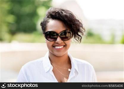 people, summer and eyewear - happy african american young woman in sunglasses outdoors. happy african american young woman in sunglasses
