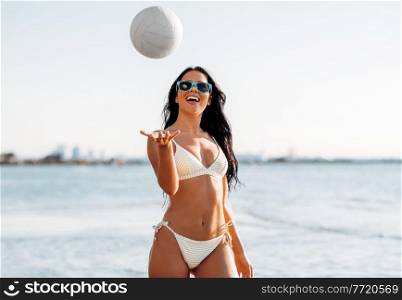 people, summer and leisure concept - happy smiling young woman in bikini swimsuit playing with volleyball on beach. woman in bikini playing with volleyball on beach