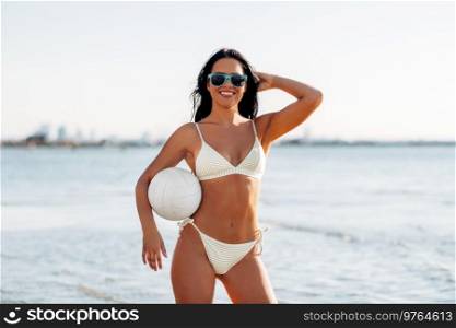 people, summer and leisure concept - happy smiling young woman in bikini swimsuit posing with volleyball on beach. woman in bikini posing with volleyball on beach