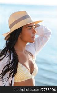 people, summer and leisure concept - portrait of young woman in bikini swimsuit, white shirt and straw hat on beach. portrait of woman in bikini and hat on beach