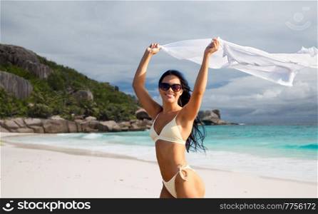 people, summer and swimwear concept - happy smiling young woman in bikini swimsuit with pareo over tropical beach background in french polynesia. woman in bikini swimsuit with cover-up on beach