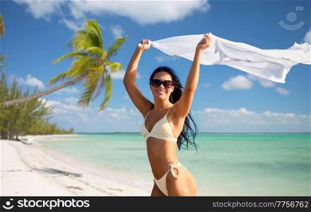 people, summer and swimwear concept - happy smiling young woman in bikini swimsuit with pareo over tropical beach background in french polynesia. woman in bikini swimsuit with pareo on beach